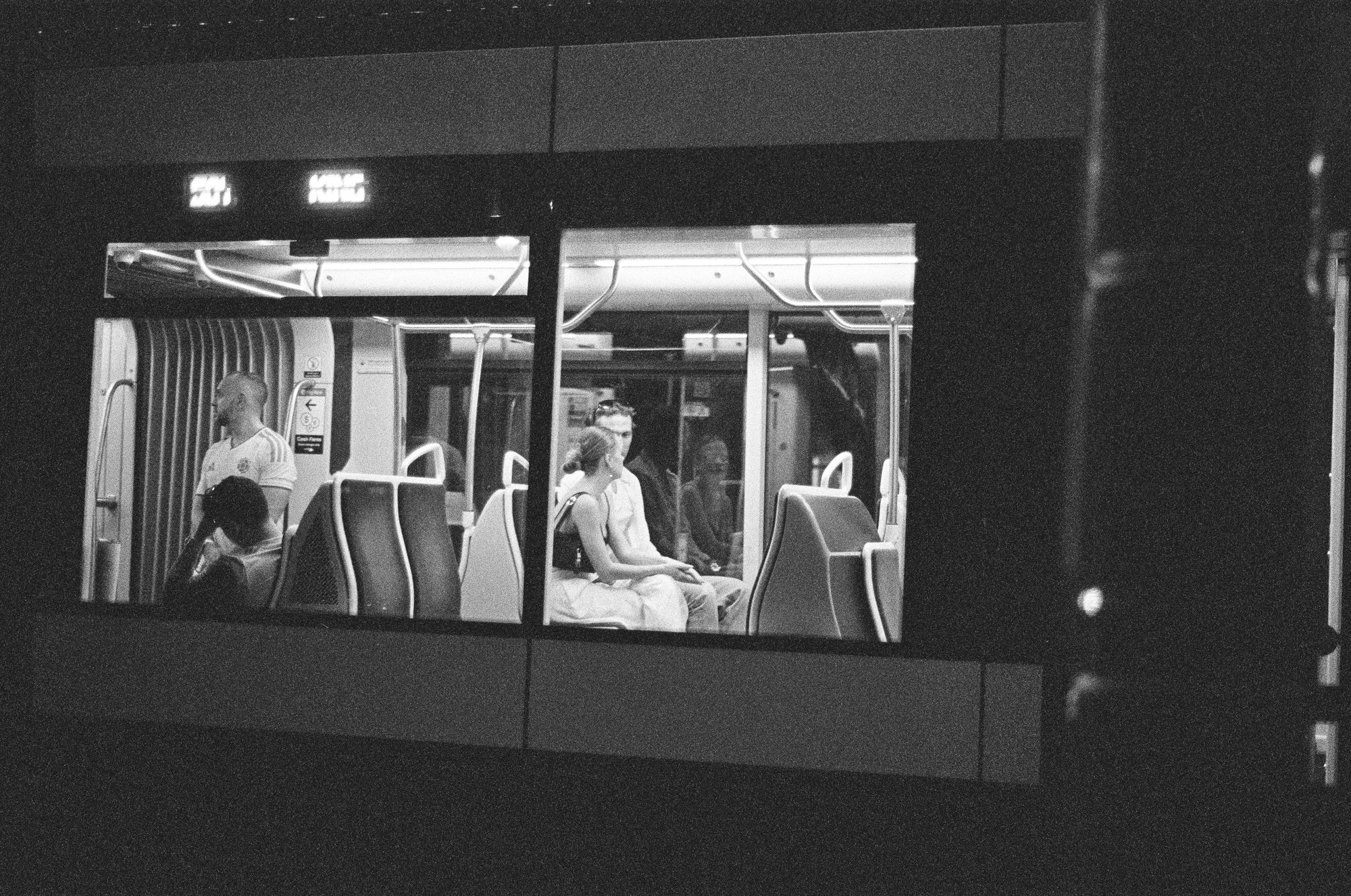 A couple seen through the lit window of a streetcar at night