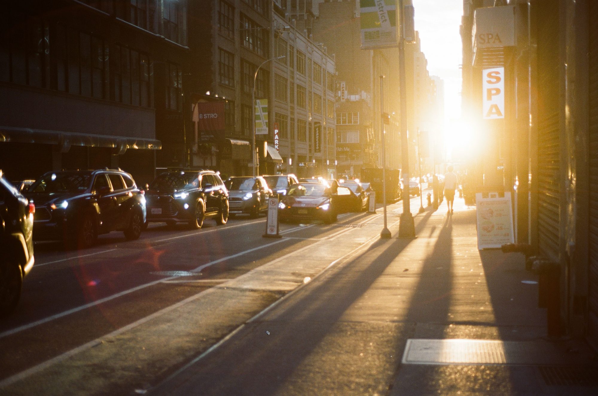 Low sun flaring down a street of parked cars, long shadows across the road