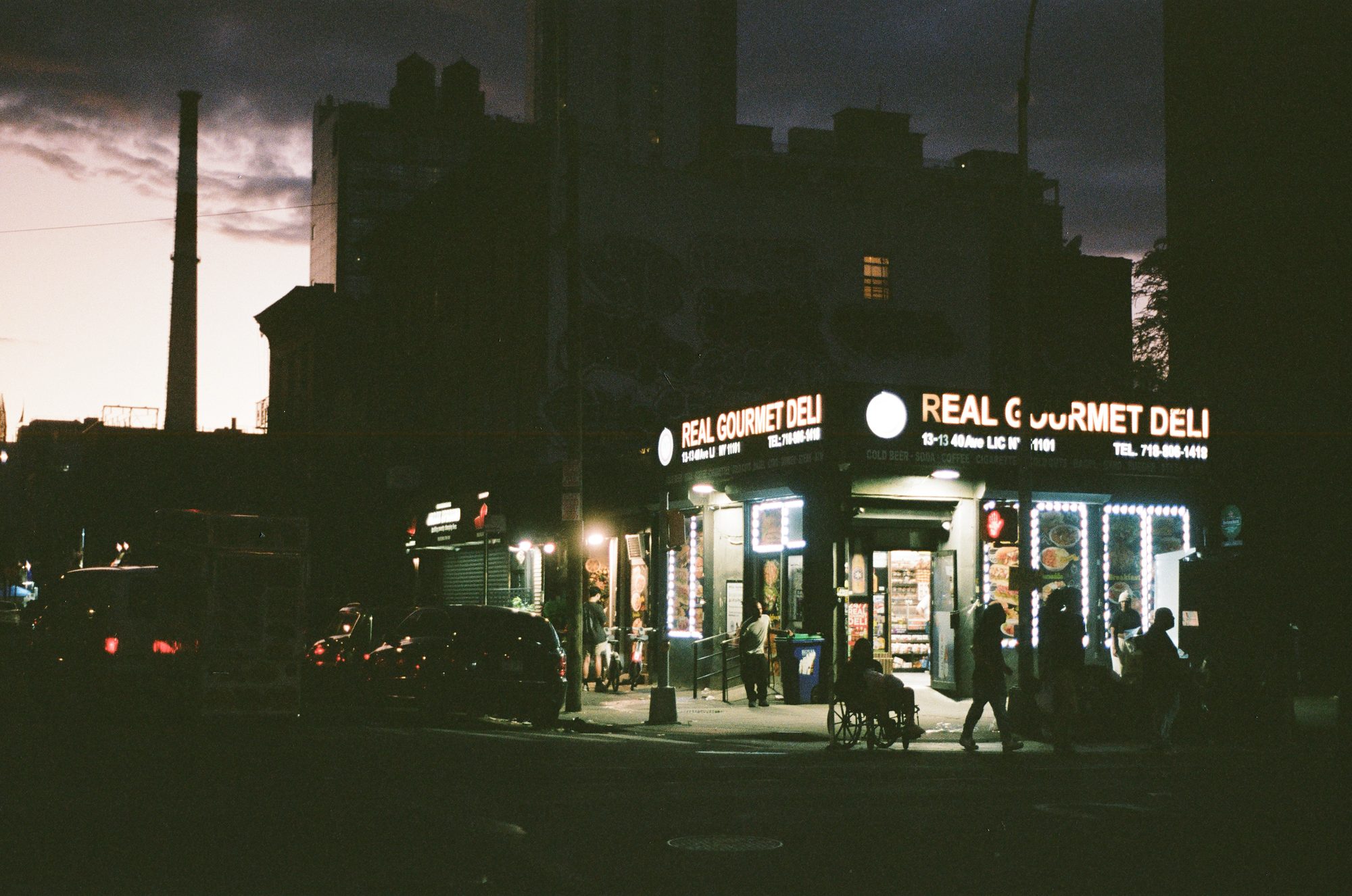 A corner deli glowing under a darkening sky