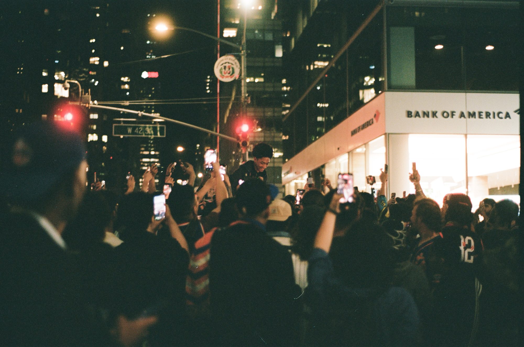 Fans holding up phones in a dark crowd at a street corner