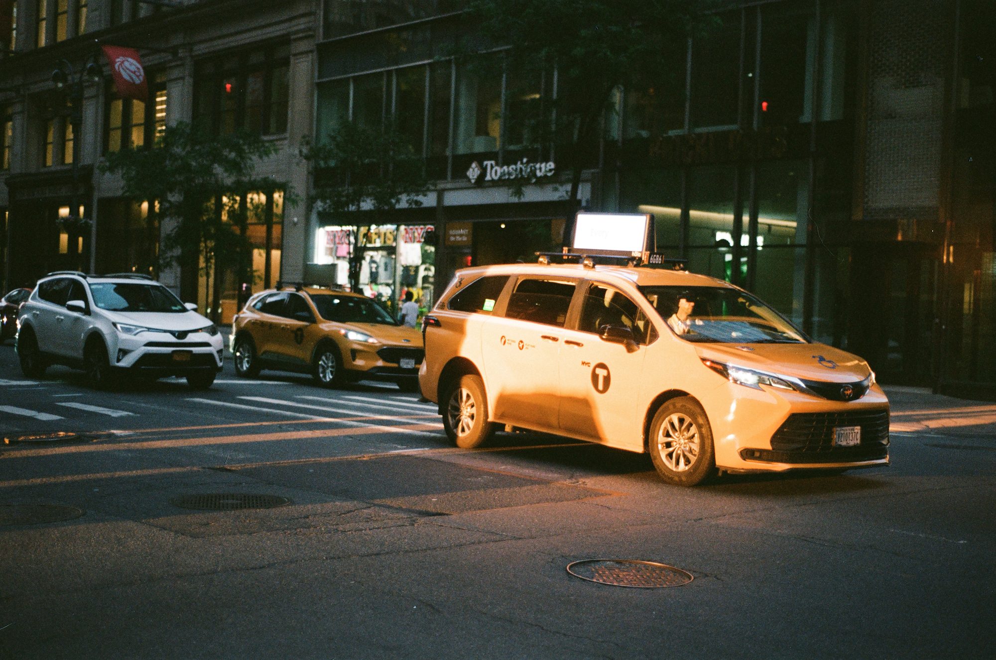 A yellow taxi turning through an intersection at dusk
