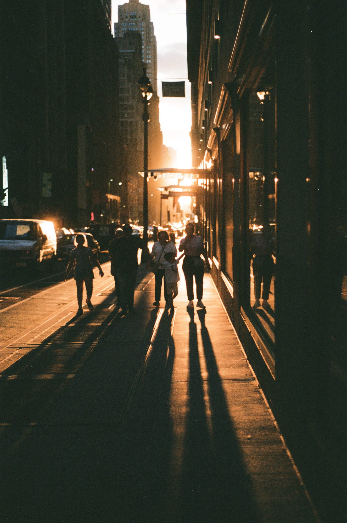 Pedestrians silhouetted as they walk into the sunset down a sidewalk