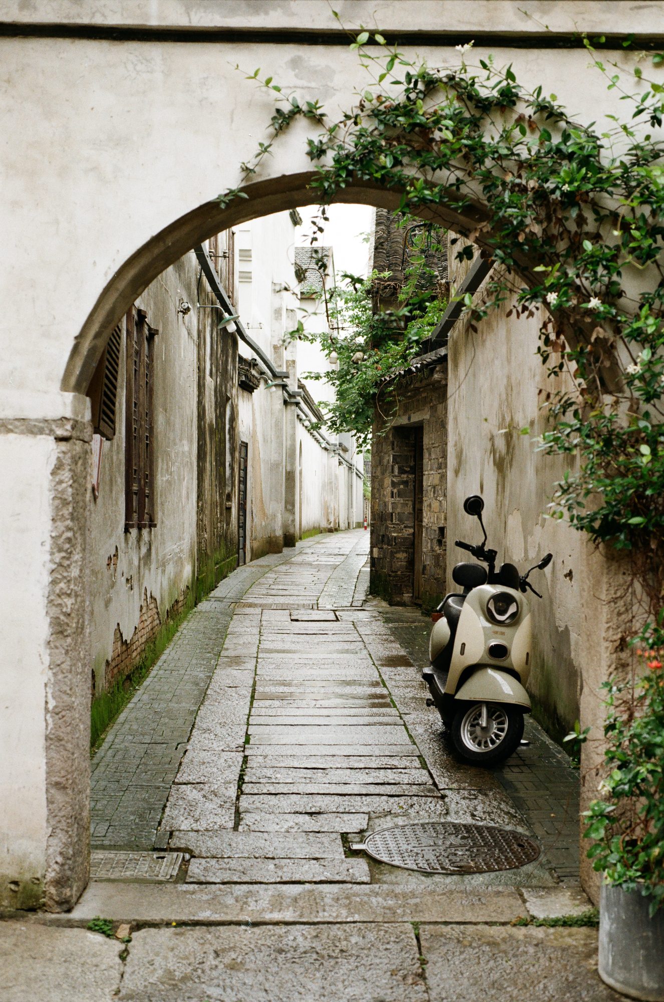 A narrow stone lane through an archway, a scooter parked inside