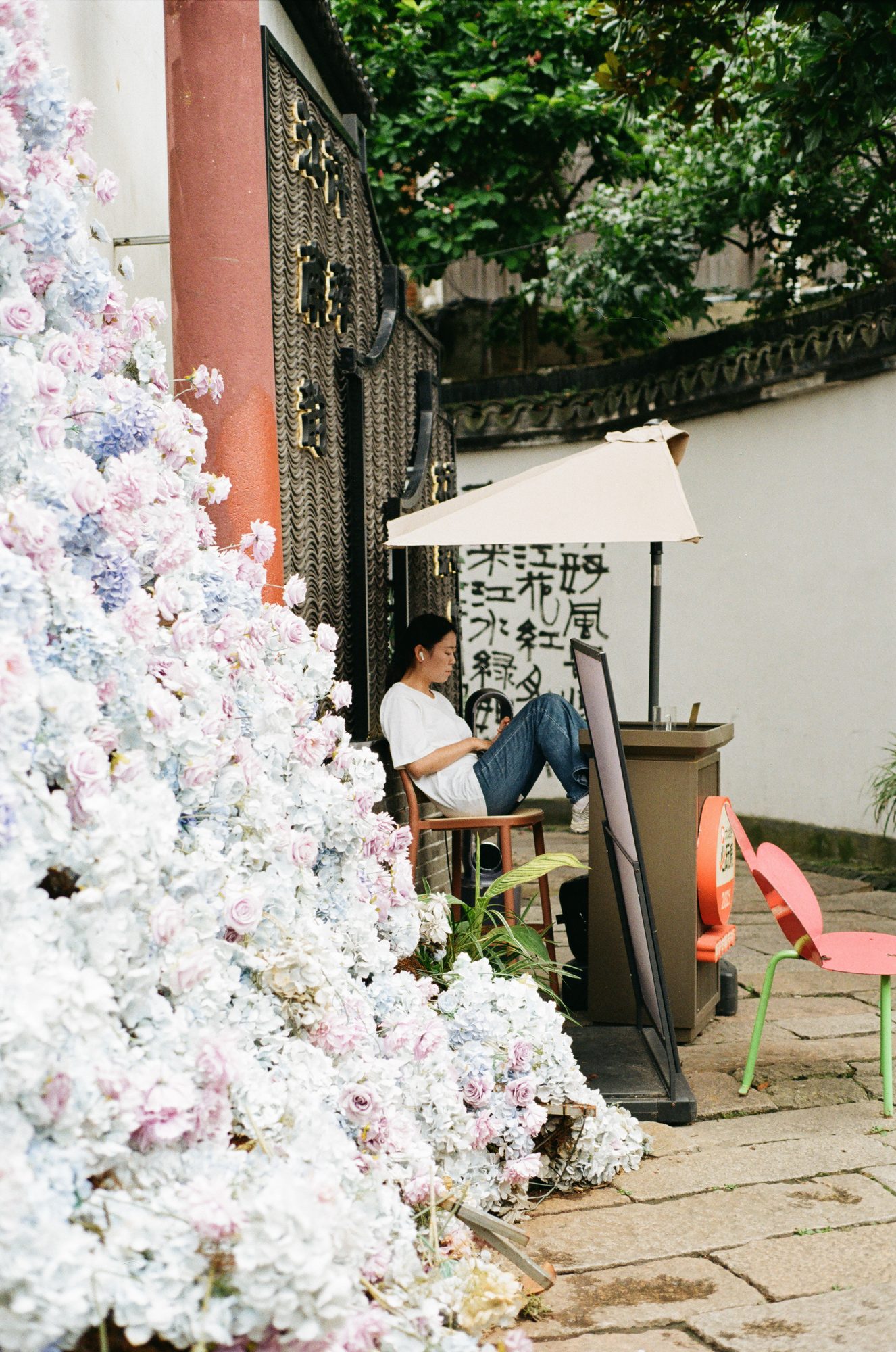 White flowers heaped against a wall beside a woman reading