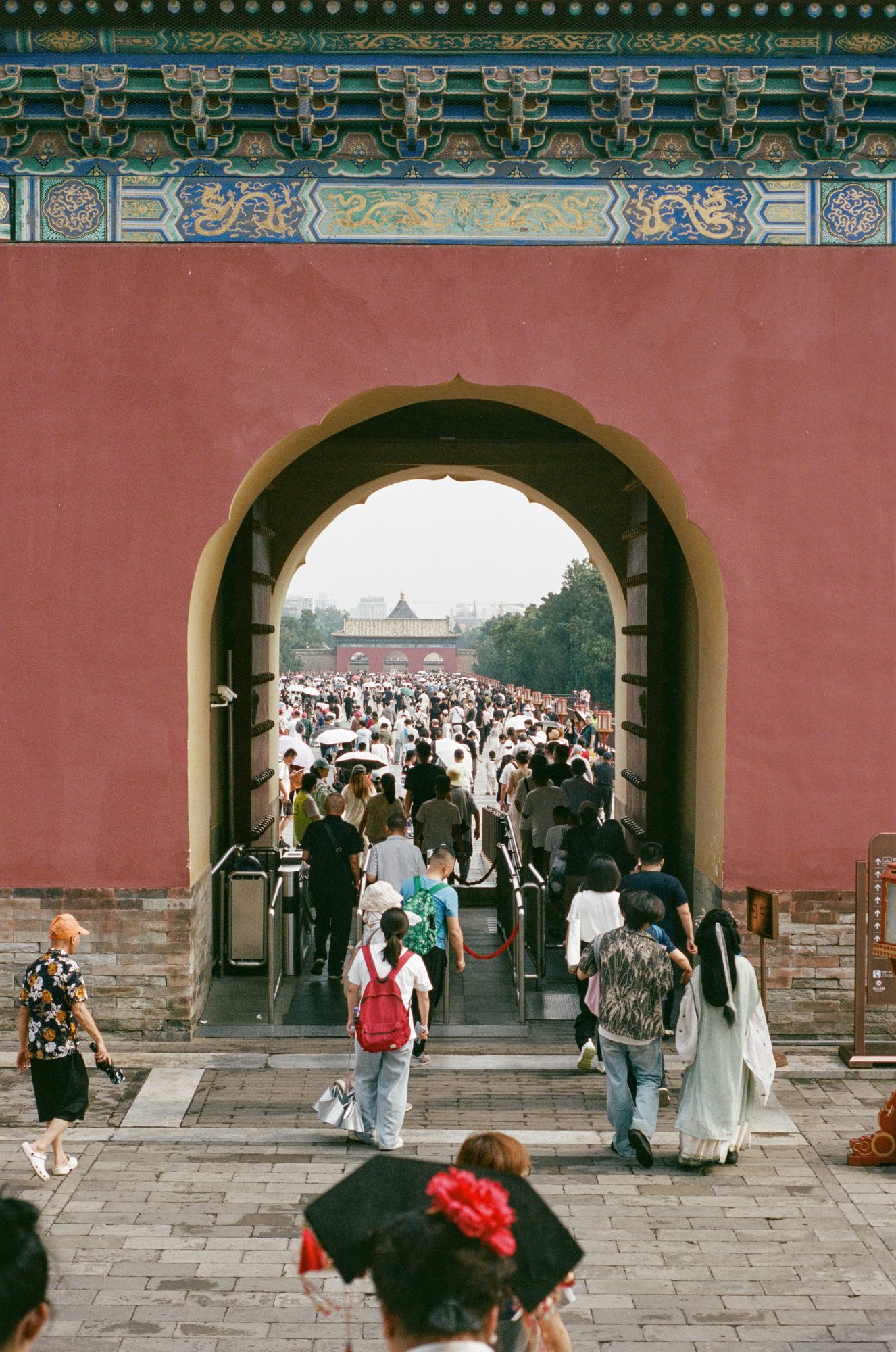 A crowd streaming through an arched gate in a red wall toward another gate beyond