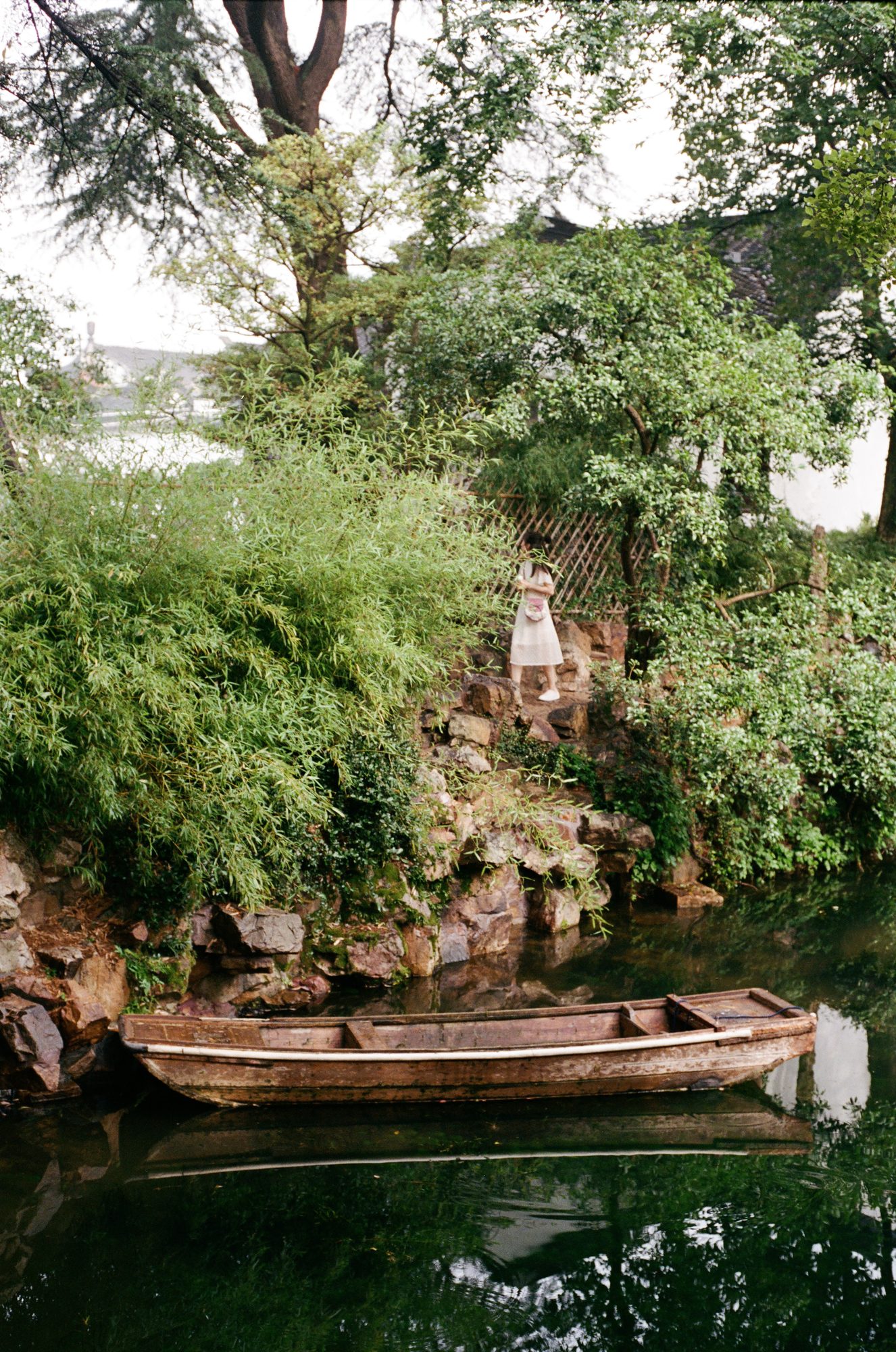 A small wooden boat in a garden pond under trees