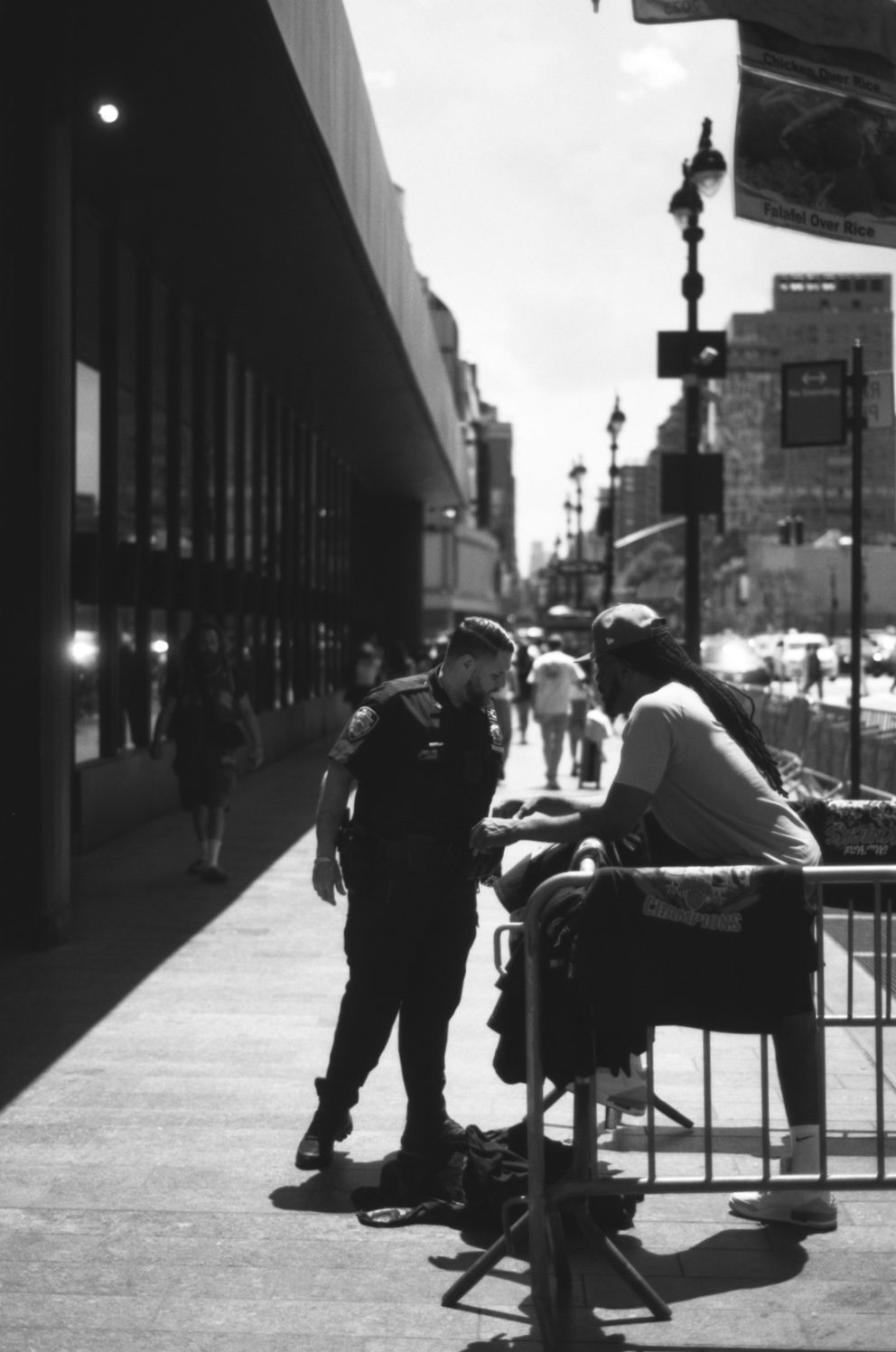 Two people talking at a railing on a sunny sidewalk