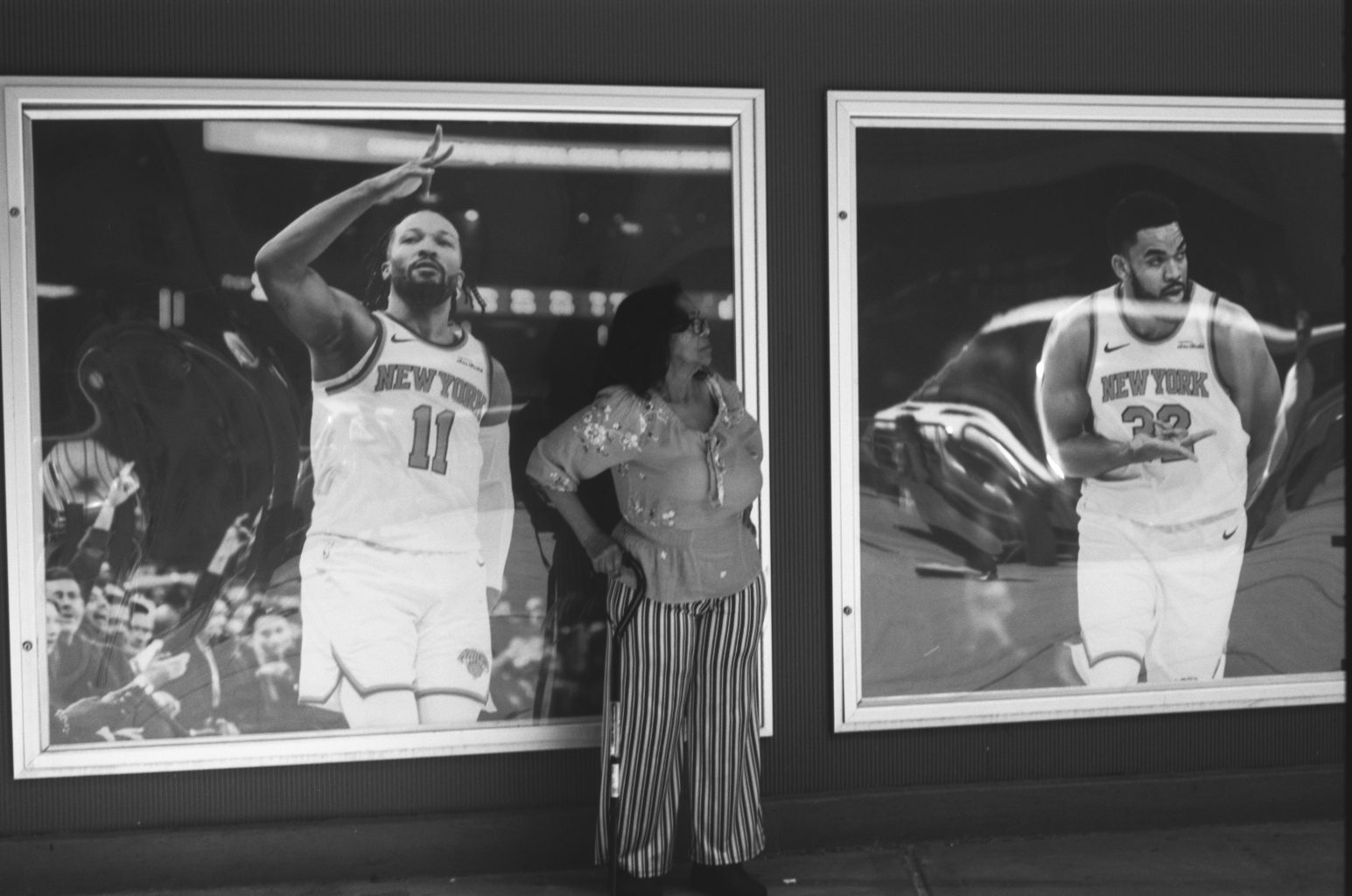 Black-and-white: a woman poses against shop-window posters of Knicks players