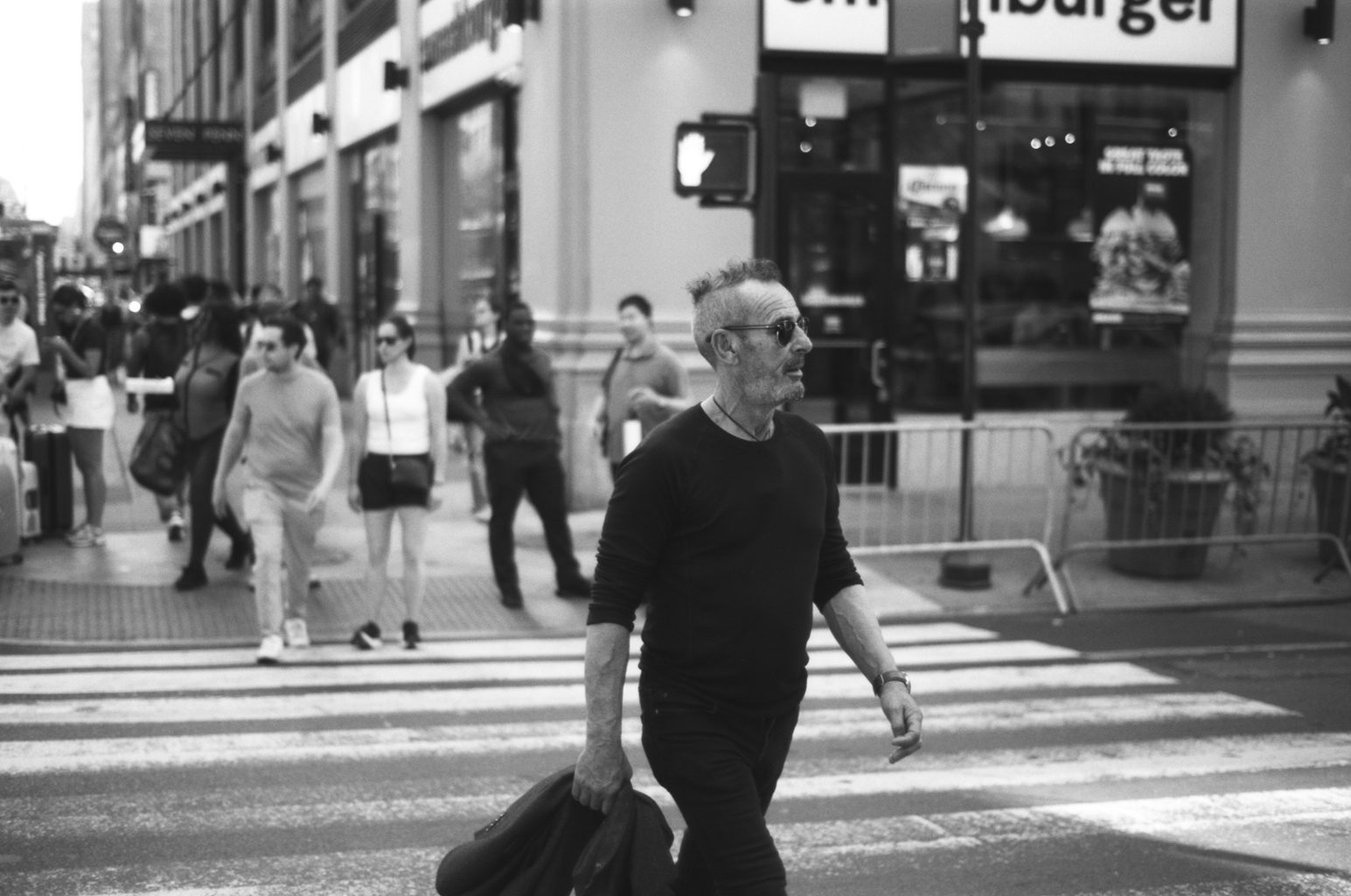 A man in black crossing the street, a crowd behind him