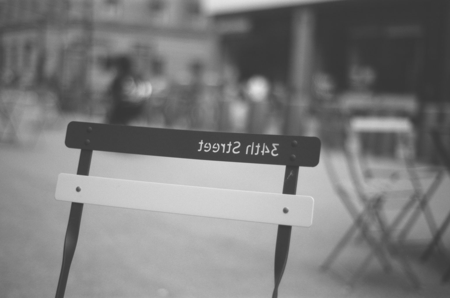 A folding café chair stamped 34th Street, the crowd blurred behind