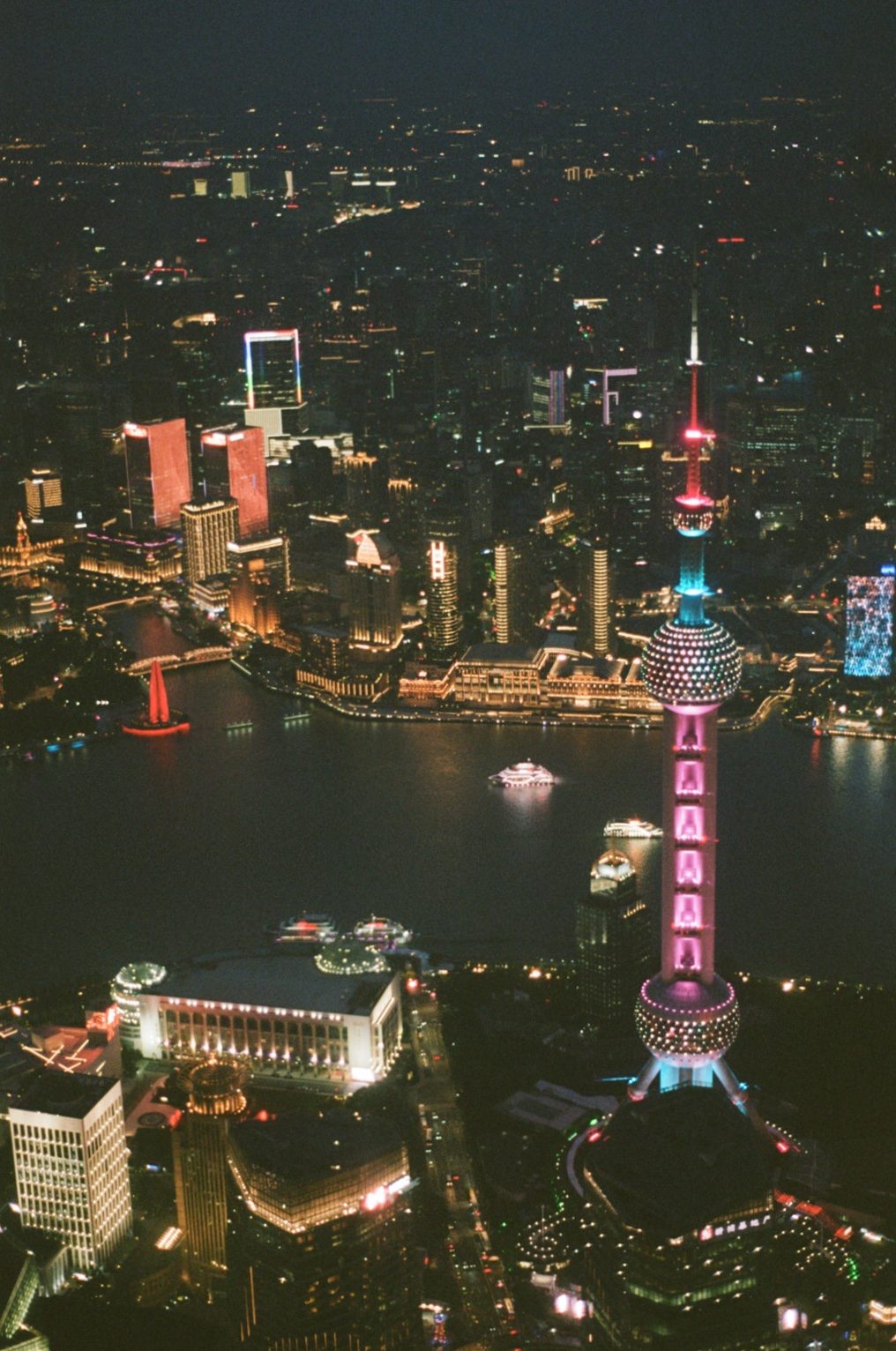 Shanghai at night from high above, the Oriental Pearl Tower lit pink over the river