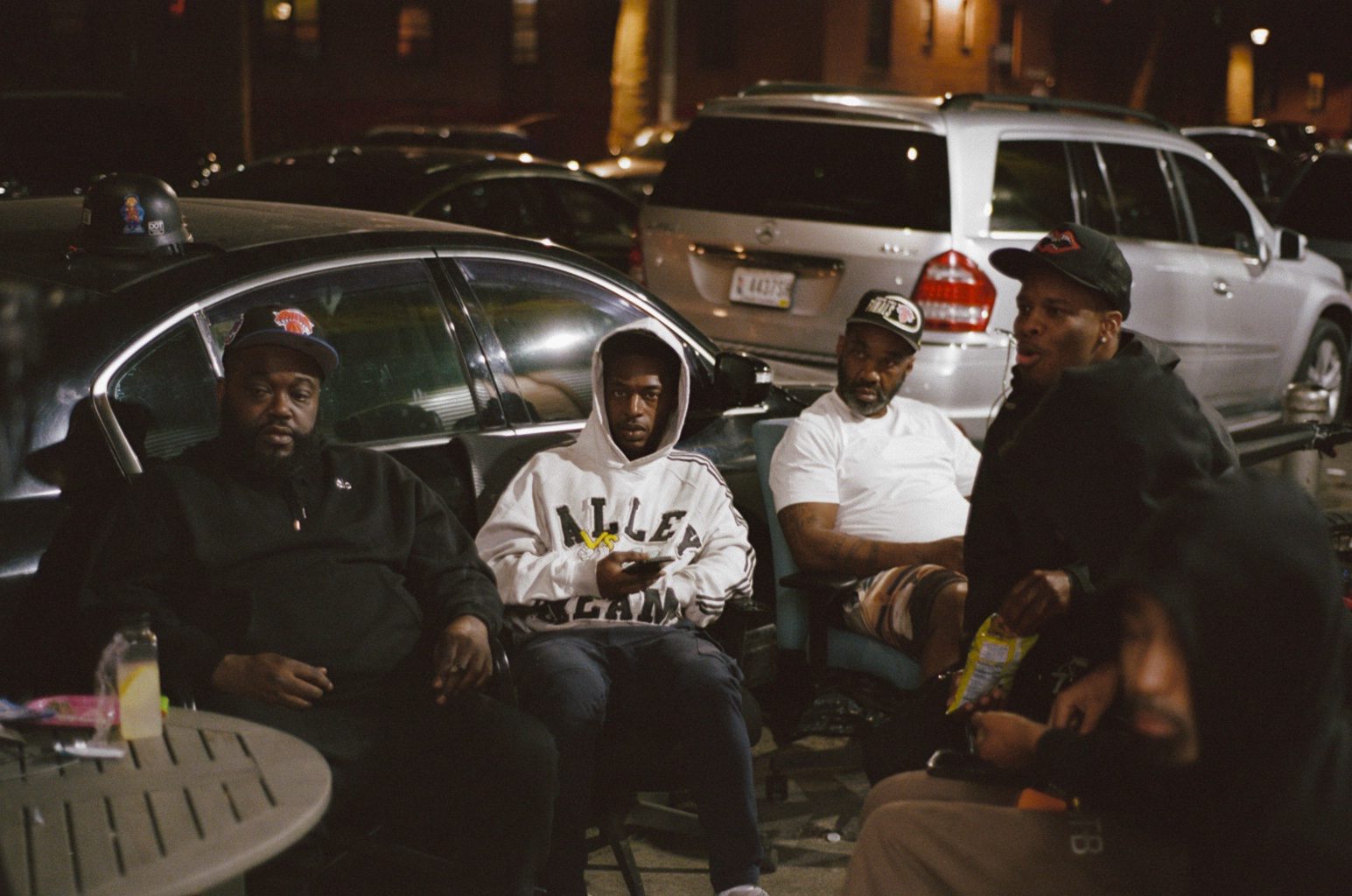 Men watching from folding chairs on a sidewalk at night