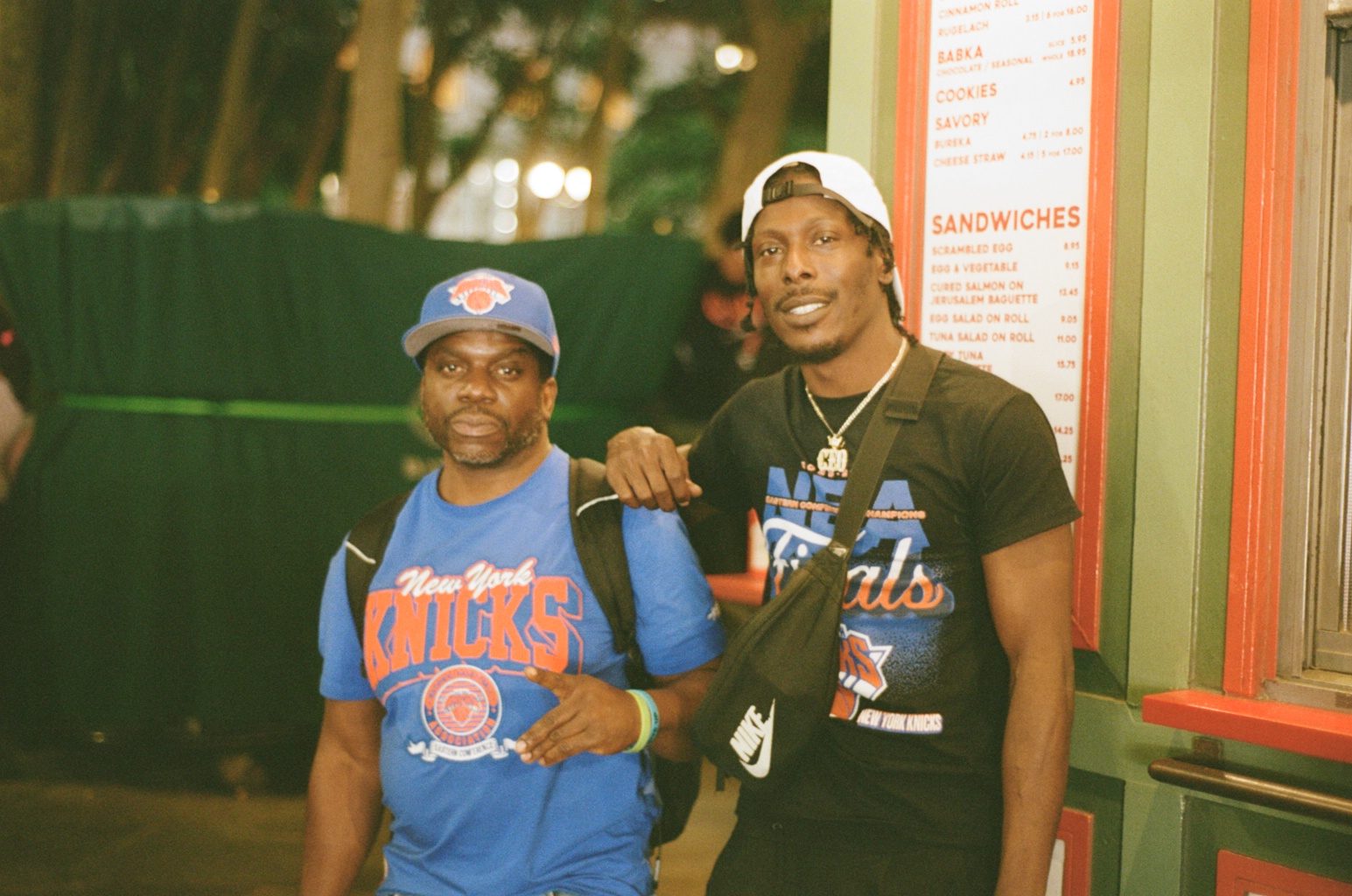 Two fans posing in Knicks shirts outside a sandwich shop